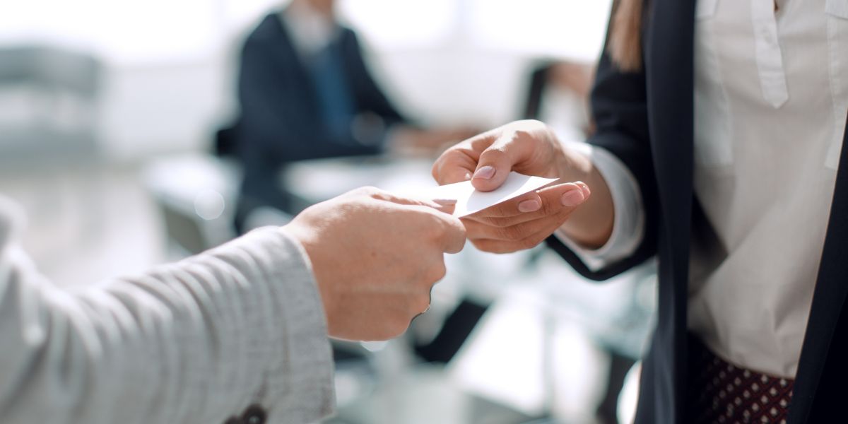Two professionals connecting at a modern networking event, one tapping an NFC business card to the other person's smartphone.