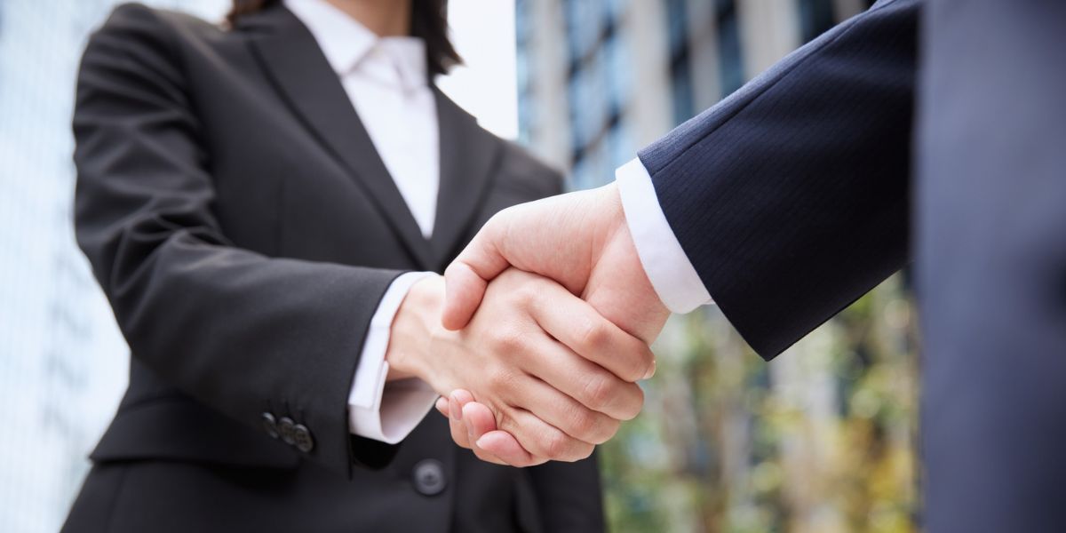 Two professionals sharing a firm handshake outside a modern office building.